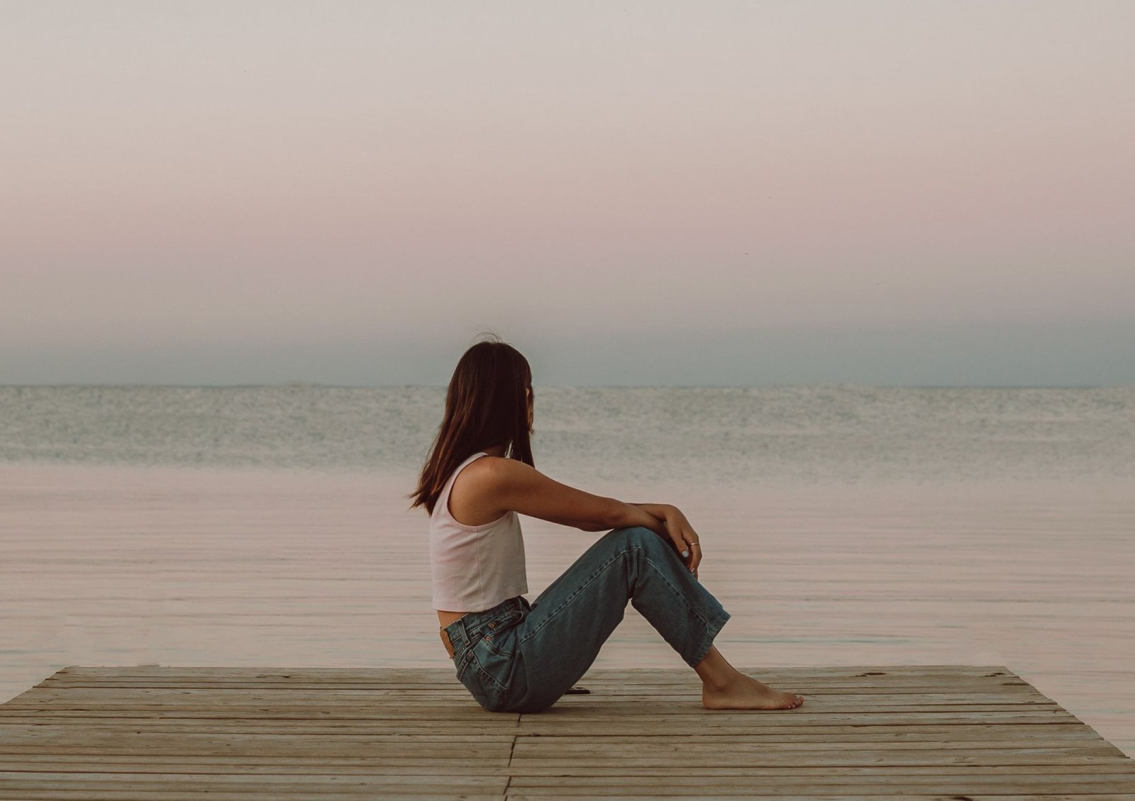 Person sits peacefully and relaxed practicing breath work to improve their wellbeing beside a beautiful body of water