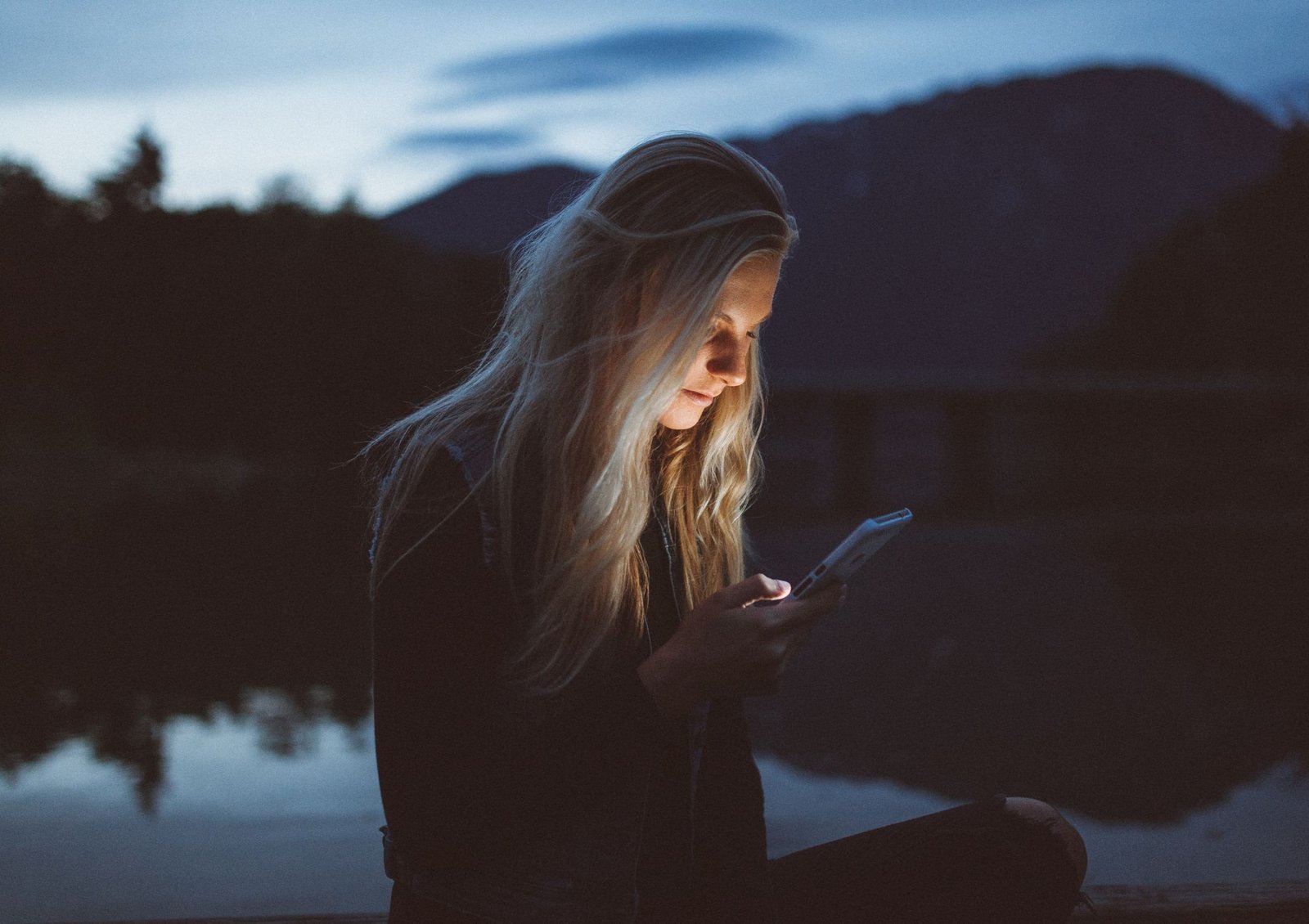 person on their mobile phone, their face lit up by the screen at night