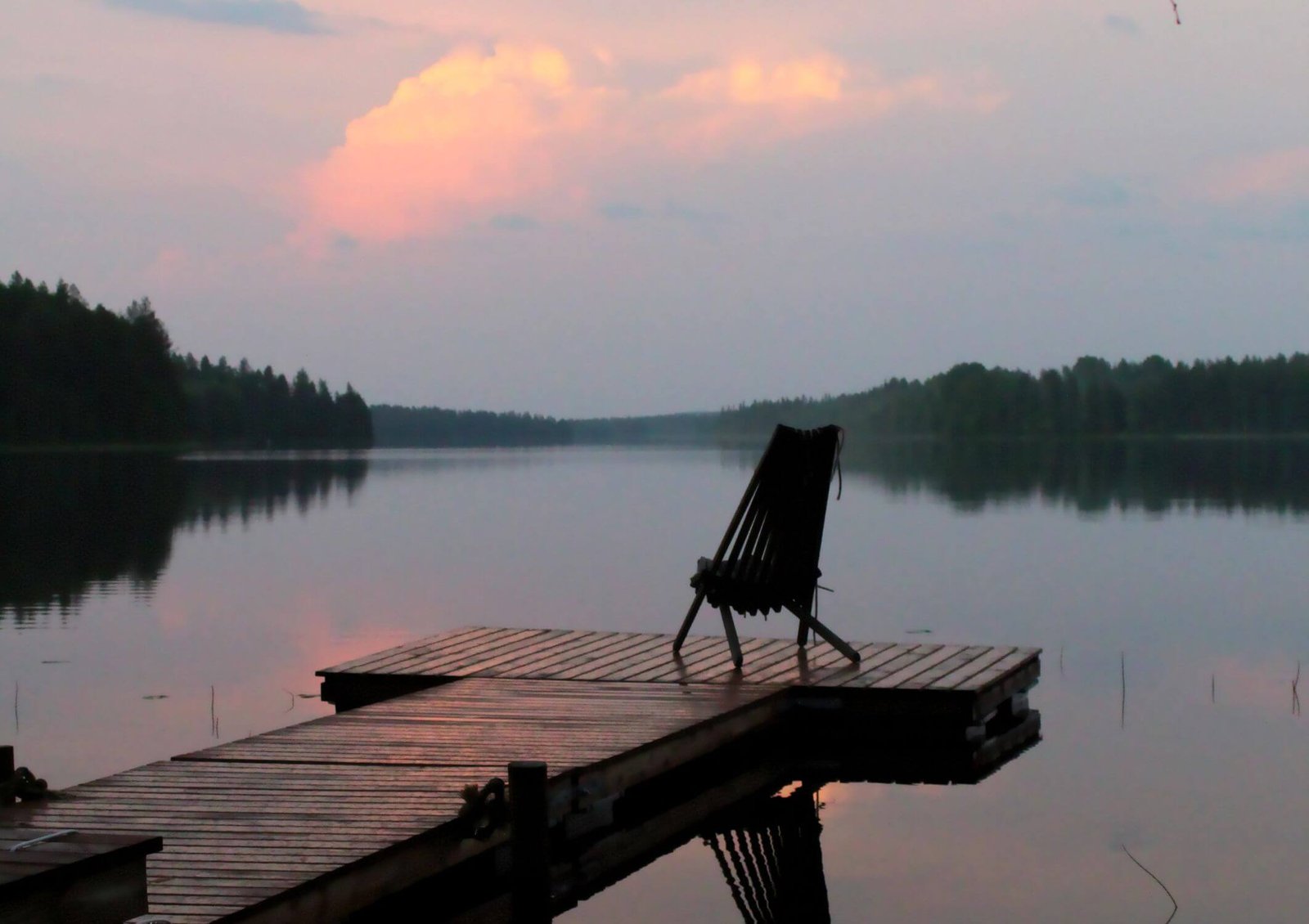 Image shows an empty chair at then of a small pier in a serene and calm environment full of stillness